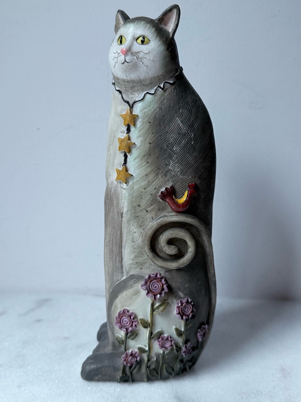 This is a whimsical resin cat figurine decorated with flowers, stars and a bird.